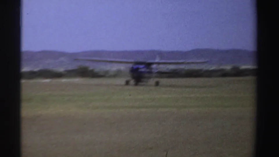 1969 Sudan 8mm frame of a small plane on the grass runway, softened by film grain and seen against distant hills.