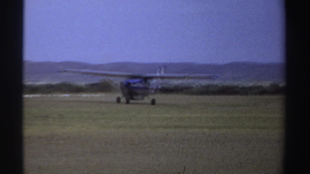 Small airplane farther right on the field, framed by dark vertical film borders.