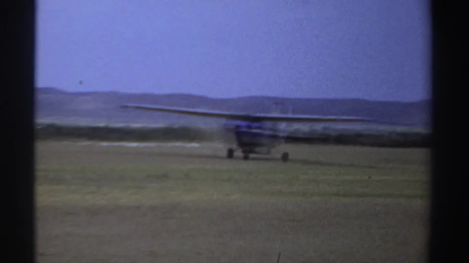 Soft 8mm frame from Sudan in 1969 showing a small airplane taxiing across a grass field with a low horizon.