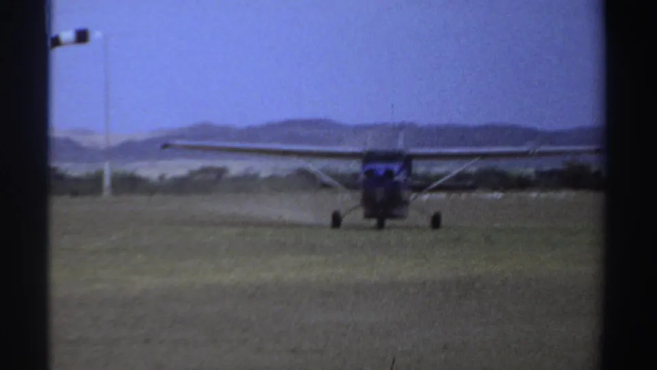 Front view of the small propeller plane on a grass runway in Sudan, with a pole fixture and distant hills visible.