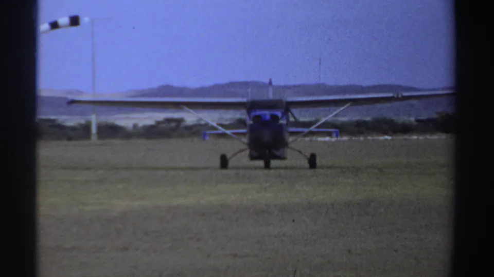 1969 Sudan 8mm frame showing a blue-and-white high-wing airplane rolling toward the camera on a grass field.