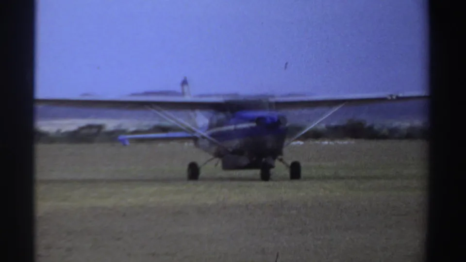 1969 Sudan 8mm frame showing the blue-and-white light plane nearing the camera and starting to turn on the grass airstrip.
