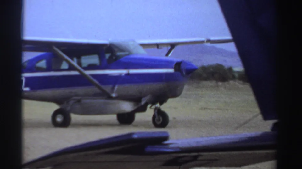 The aircraft passes close to the camera near the end of the clip, partly framed by dark film edges and foreground obstruction.