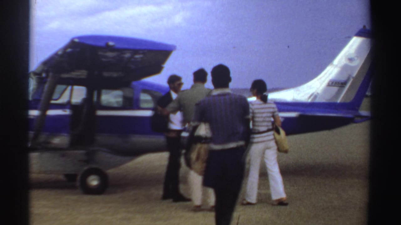 Passengers appear beside a small blue-and-white aircraft in Sudan, with bags gathered near the plane during a 1969 travel scene.