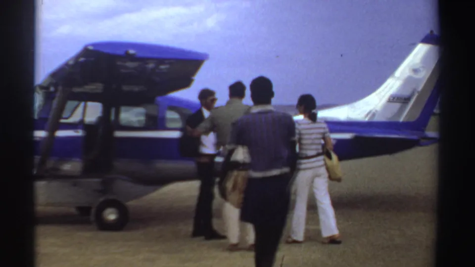 Passengers appear beside a small blue-and-white aircraft in Sudan, with bags gathered near the plane during a 1969 travel scene.