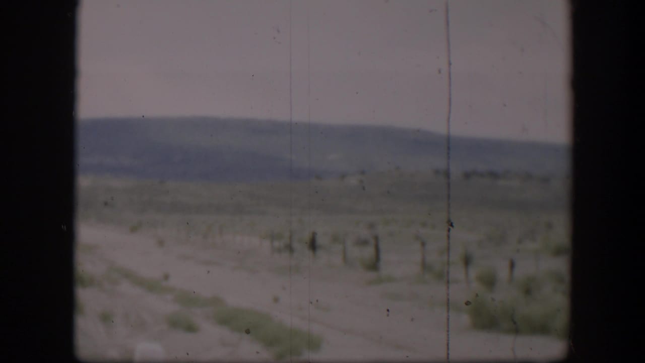 1951 Utah desert road view with sparse brush, distant hills, pale sky, and dark framing from a vehicle or window.