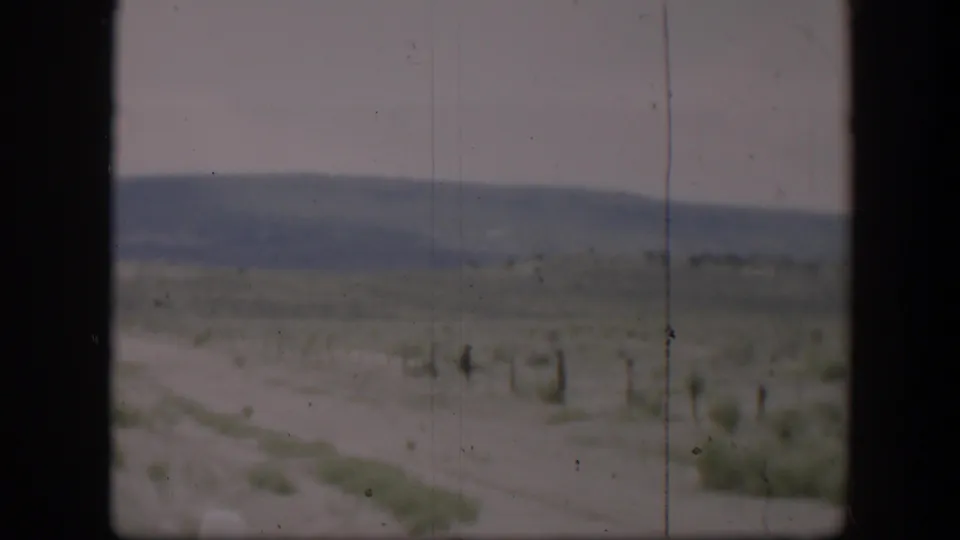 1951 Utah desert road view with sparse brush, distant hills, pale sky, and dark framing from a vehicle or window.