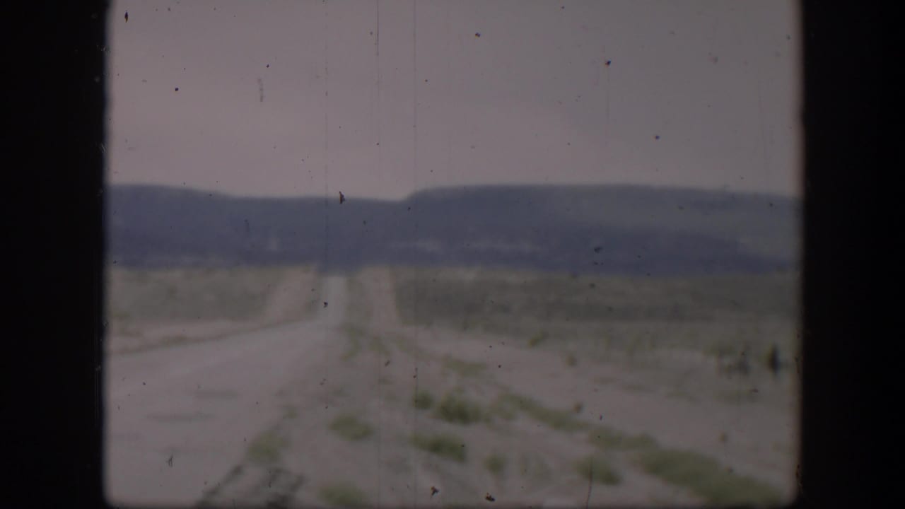 Long pale road runs through open desert toward low hills.