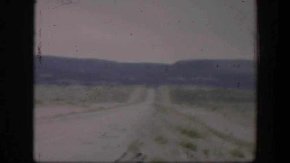 Soft 8mm view of a desert road in Utah, with scrubby flats, a distant ridge, and visible film wear.