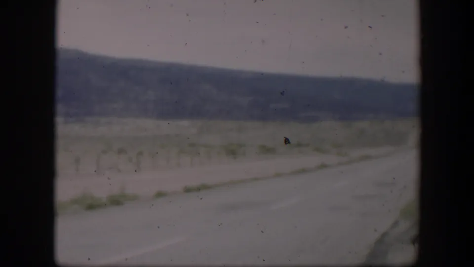 Utah desert roadside in 1951 with sandy track, low vegetation, distant hills, and visible 8mm dust and scratches.