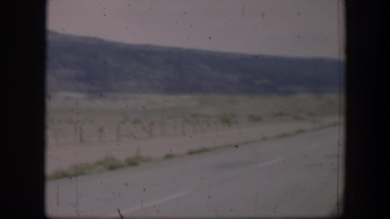 1951 Utah home-movie view of a roadside field, wire fence posts, and distant low hills seen through a vehicle window.