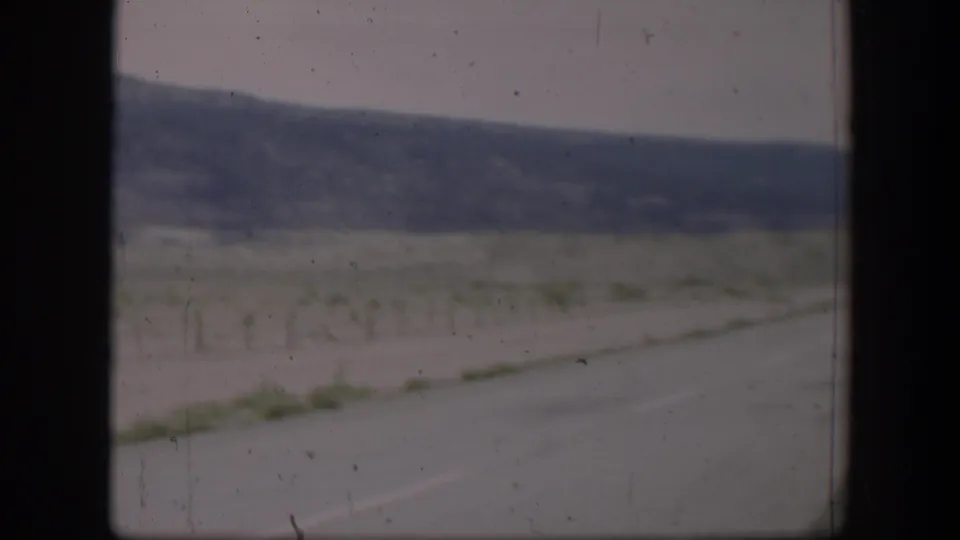 1951 Utah home-movie view of a roadside field, wire fence posts, and distant low hills seen through a vehicle window.