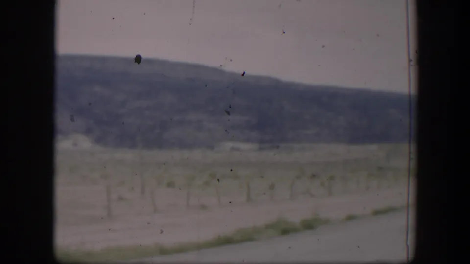1951 Utah roadside view showing a fenced open field, low hills, pale sky, and dark vertical window framing.