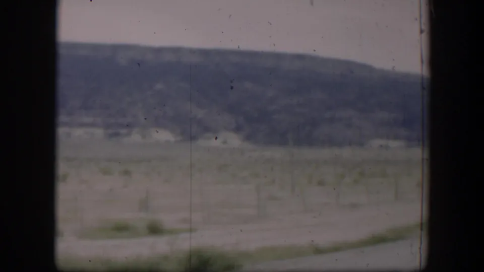 1951 Utah 8mm frame with a soft roadside field, wire fence line, low hills, and dark vehicle-window borders.