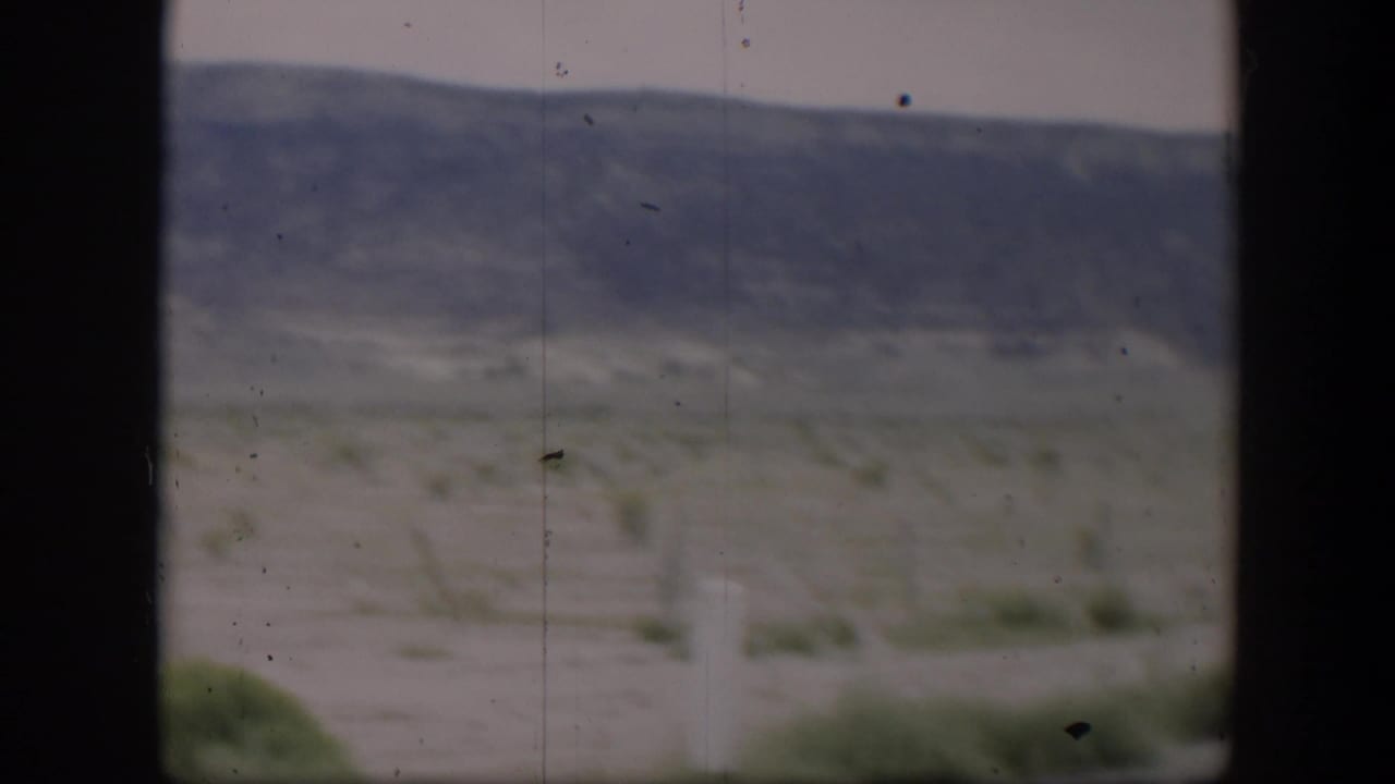1951 Utah 8mm frame showing muted desert terrain with sparse bushes and distant mountain ridges behind dark window-like edges.