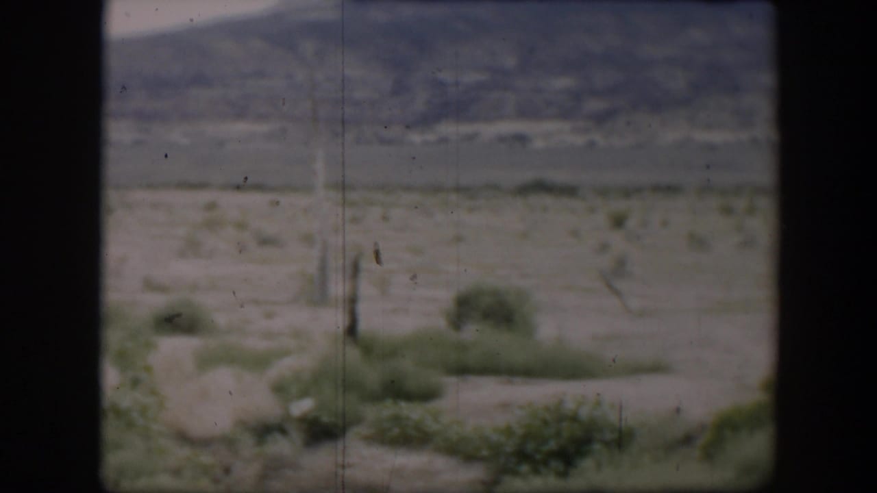 1951 Utah 8mm view of pale ground, green roadside bushes, and a distant mountain slope within a dark window-like frame.