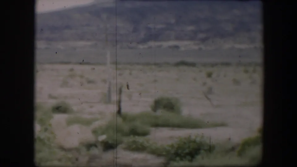 1951 Utah 8mm view of pale ground, green roadside bushes, and a distant mountain slope within a dark window-like frame.