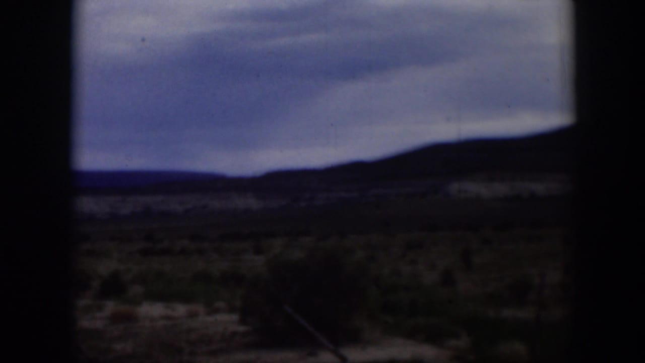 1951 Utah frame showing a darker arid landscape with low brush, silhouetted ridge, and cloudy sky in soft 8mm color.