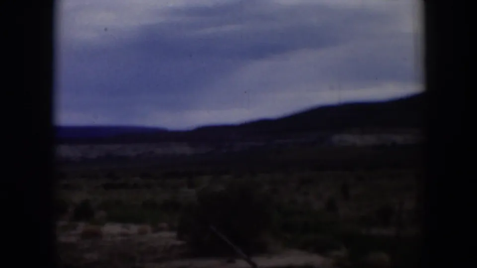 1951 Utah frame showing a darker arid landscape with low brush, silhouetted ridge, and cloudy sky in soft 8mm color.