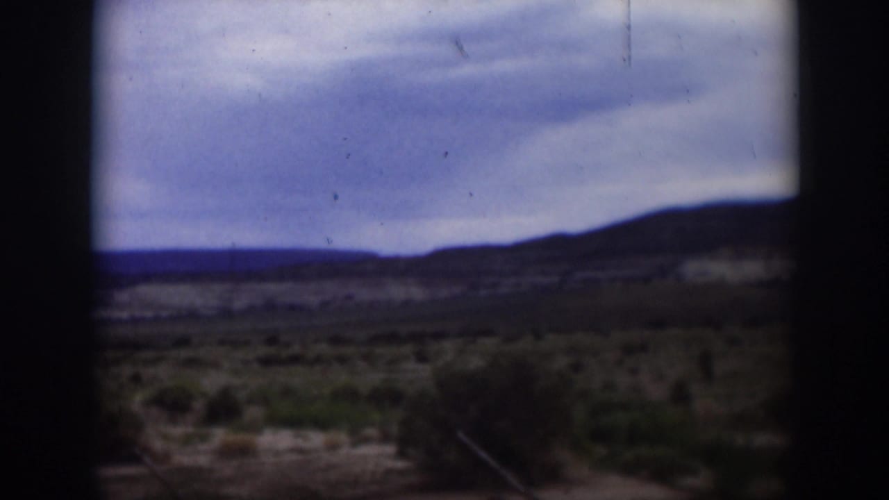 1951 Utah 8mm frame showing a cloudy sky over scrubby desert ground and low distant hills, partially obscured by dark film borders.