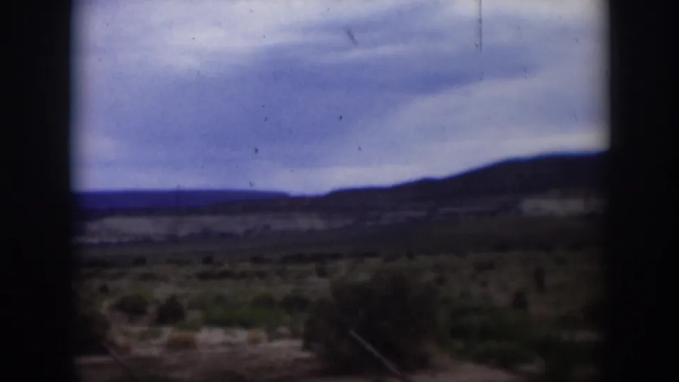 1951 Utah 8mm frame showing a cloudy sky over scrubby desert ground and low distant hills, partially obscured by dark film borders.