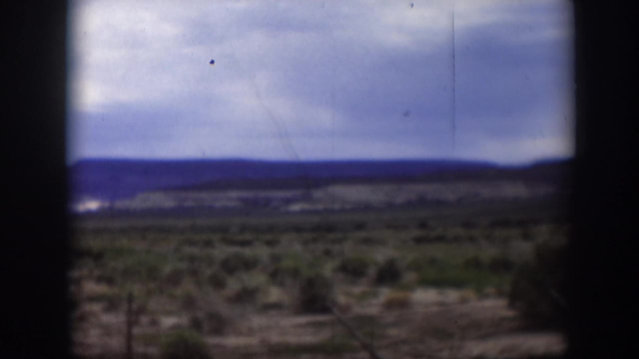 1951 Utah home-movie frame with a dark vertical film edge crossing a broad scrub plain and blue-gray mountain ridge under clouds.