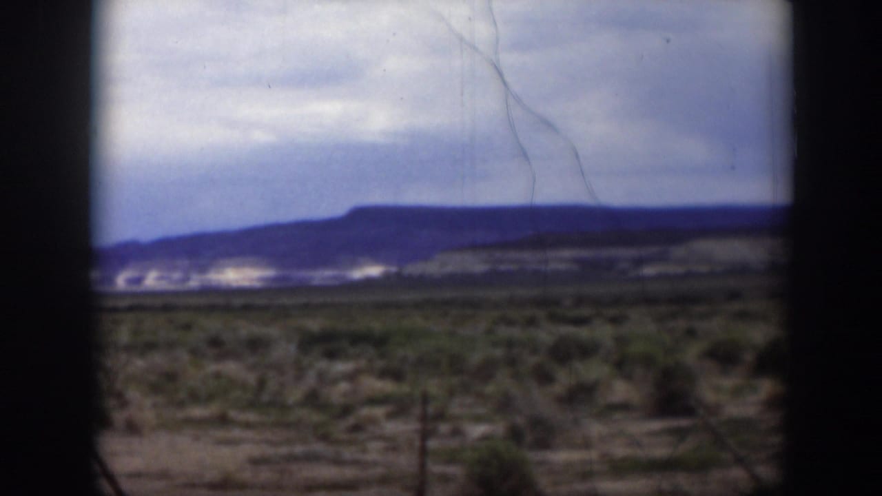 1951 Utah 8mm frame showing distant hills and pale exposed slopes beyond dry scrubland, with scratches and soft home-movie focus.