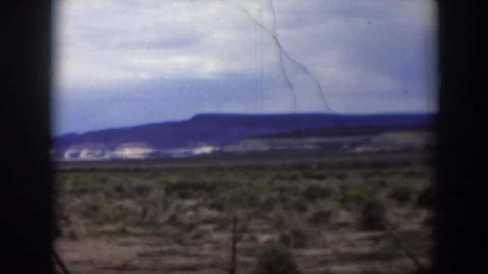 1951 Utah 8mm frame showing distant hills and pale exposed slopes beyond dry scrubland, with scratches and soft home-movie focus.