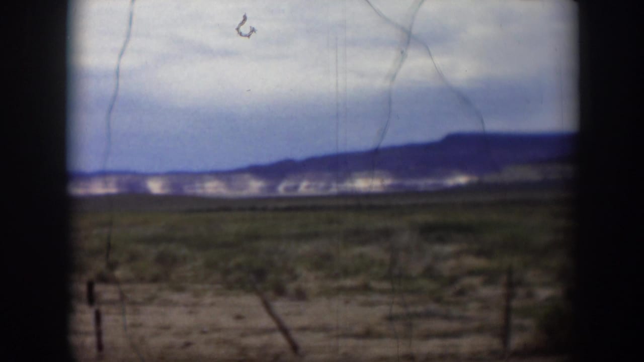 1951 Utah home-movie view across scrubby desert ground toward distant hills, seen through dark window or vehicle edges.
