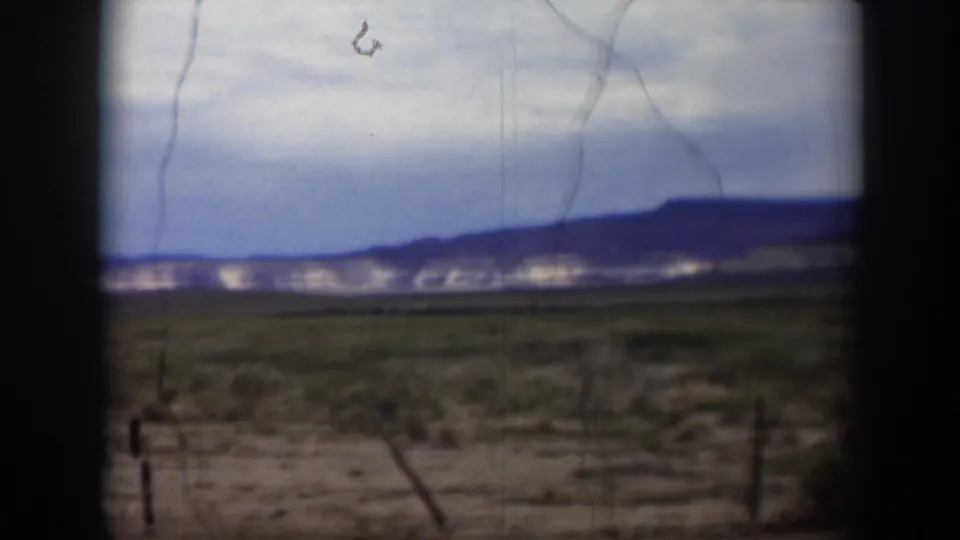 1951 Utah home-movie view across scrubby desert ground toward distant hills, seen through dark window or vehicle edges.