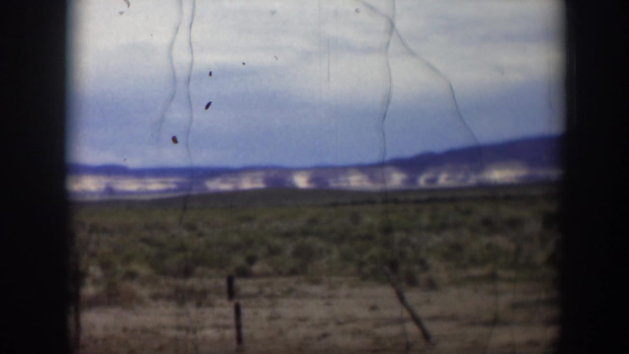 Utah landscape in a 1951 8mm frame, showing low desert greenery, distant hills, clouds, and dark foreground edges.