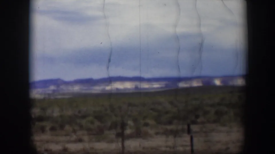 Soft 8mm view of Utah desert vegetation and fence posts with blue hills in the distance beneath a pale clouded sky.
