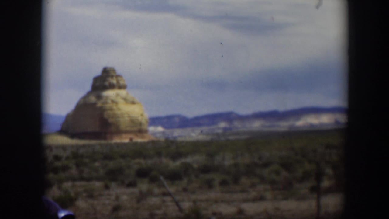 Dark vehicle frame around a tan rock formation in a scrub desert landscape.