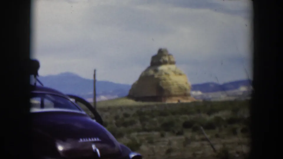 1951 Utah 8mm frame showing part of a dark sedan, scrubland, distant hills, and a layered desert butte-like formation.