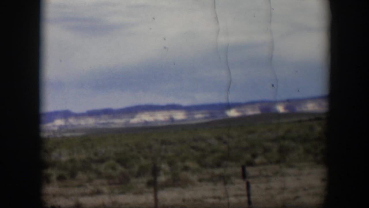 Late frame from 1951 Utah 8mm footage showing open scrubland, fence posts, distant hills, clouds, and no visible people.