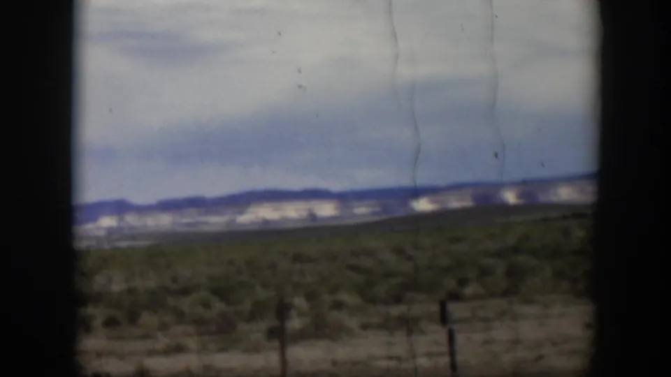 Late frame from 1951 Utah 8mm footage showing open scrubland, fence posts, distant hills, clouds, and no visible people.