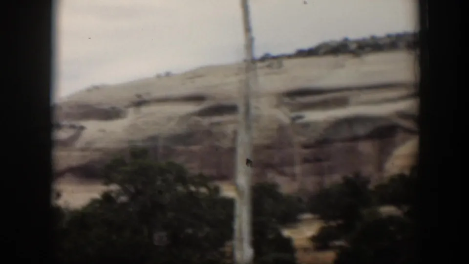 Utah sandstone cliffs and eroded pale rock faces pass by in soft-focus 8mm footage, with shrubs along the lower edge of frame.