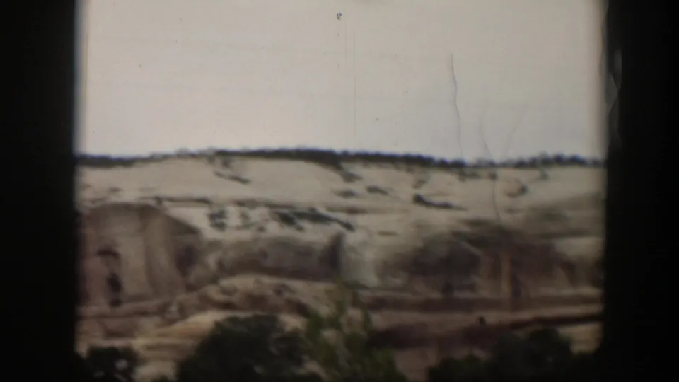 A broad Utah sandstone slope fills the frame, with sparse vegetation at the base and home-movie film marks visible over the pale sky.