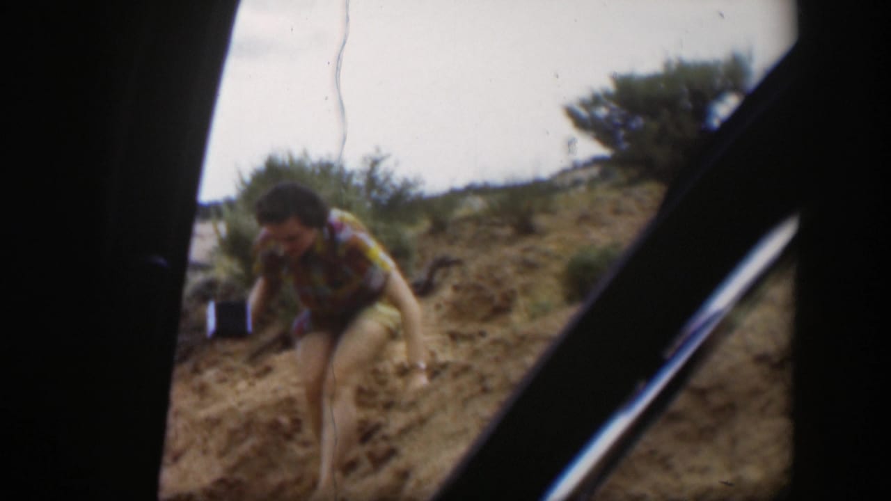 1951 Utah home-movie frame showing a person in patterned clothing stepping downhill on sandy terrain, partly framed by a vehicle interior.