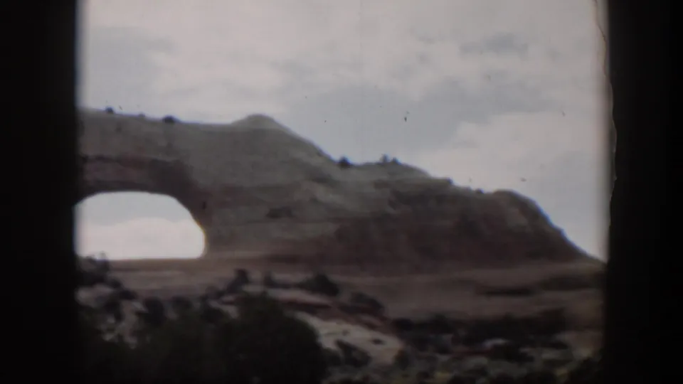 1951 Utah home-movie view of a large natural rock arch under a pale sky, with dark vehicle-window framing in the foreground.