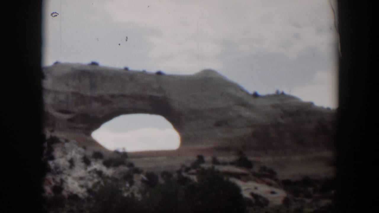 Utah 1951 8mm frame with a natural rock arch, scrubby desert foreground, pale sky, and dark vehicle-window edges.