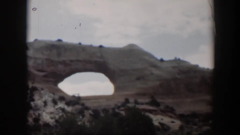Utah 1951 8mm frame with a natural rock arch, scrubby desert foreground, pale sky, and dark vehicle-window edges.