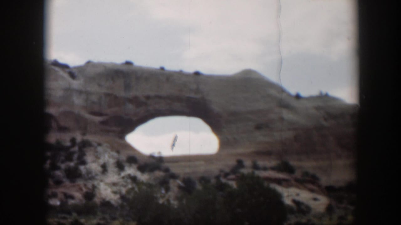 Distant natural rock arch in a desert landscape with dark film borders.