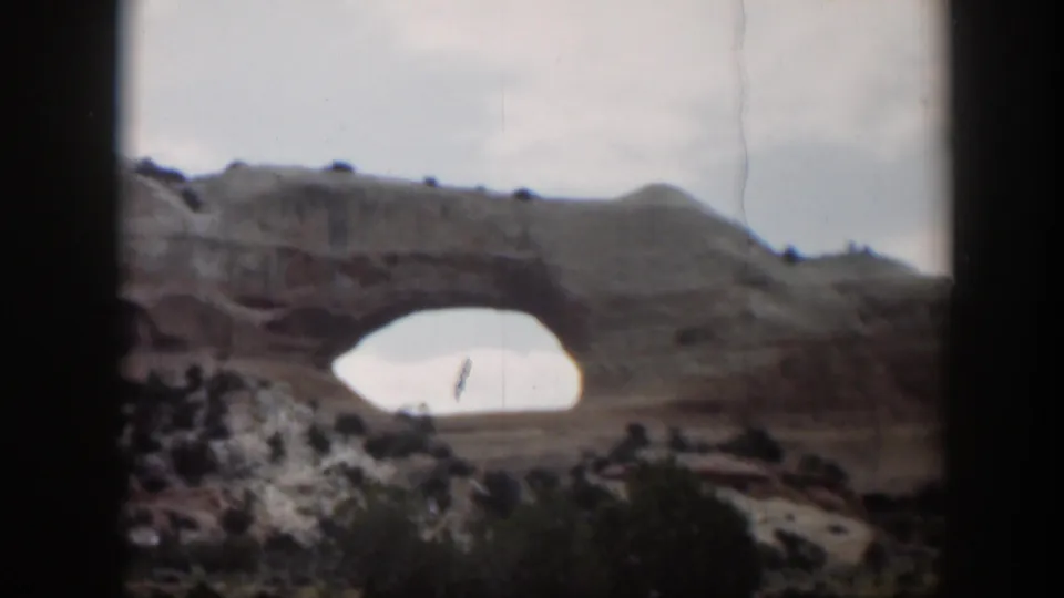1951 Utah 8mm frame showing a distant sandstone arch across pale desert terrain, with soft focus and visible film gate edges.