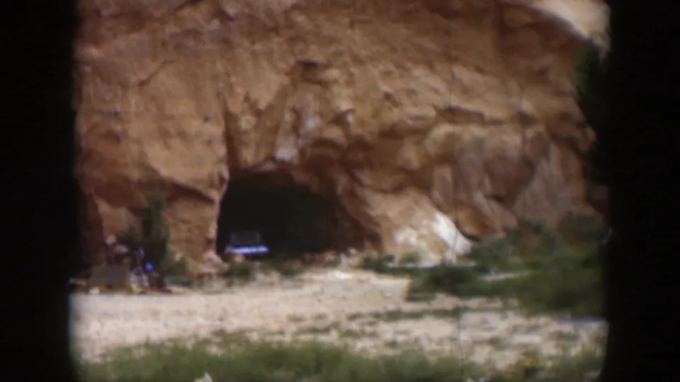 1951 Utah home-movie frame showing a sandstone rock face with two dark cave-like openings and sparse vegetation at the base.