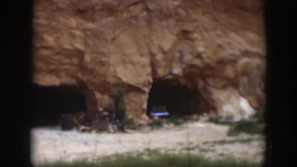 1951 Utah frame showing cave-like openings in a reddish rock face, with a parked car near the right opening.