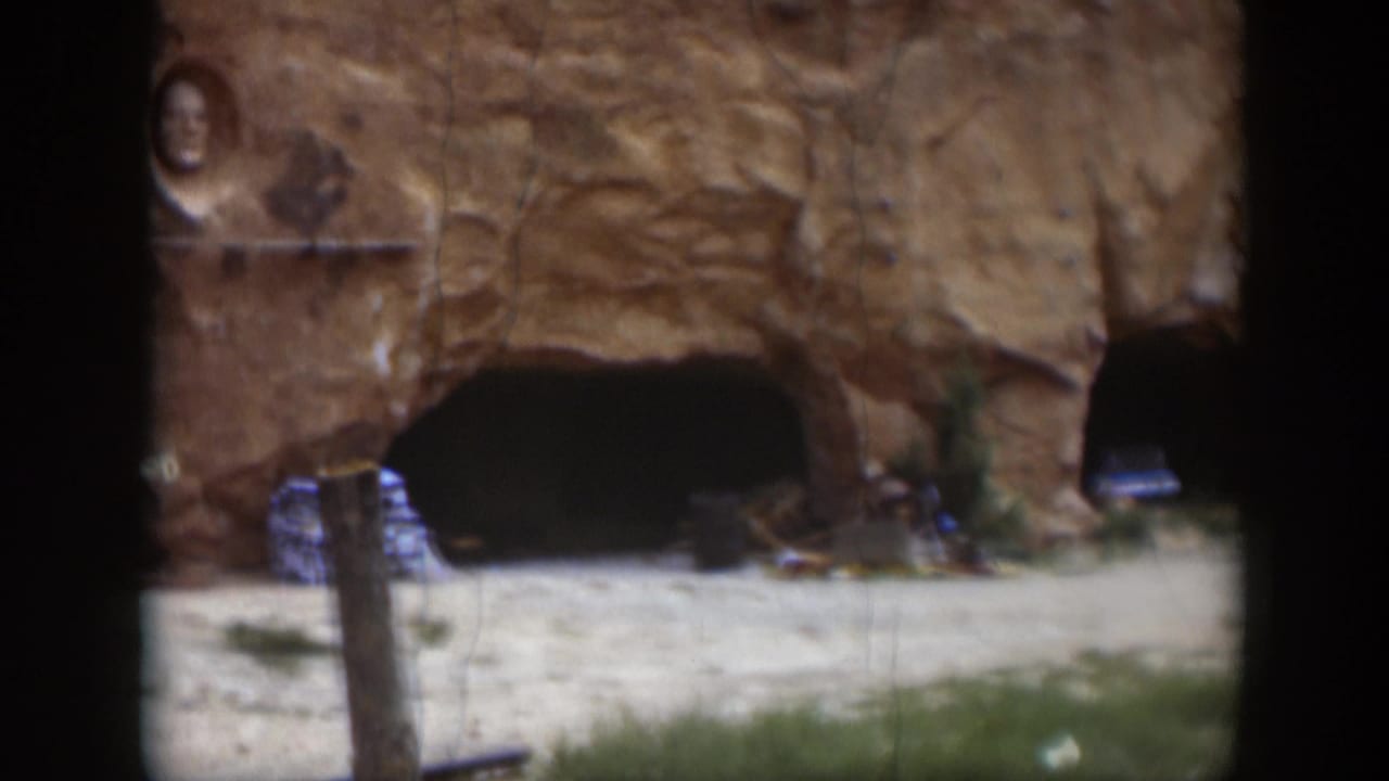 1951 Utah frame showing a large cave-like opening, a parked car partly visible at the right edge, and a foreground post.