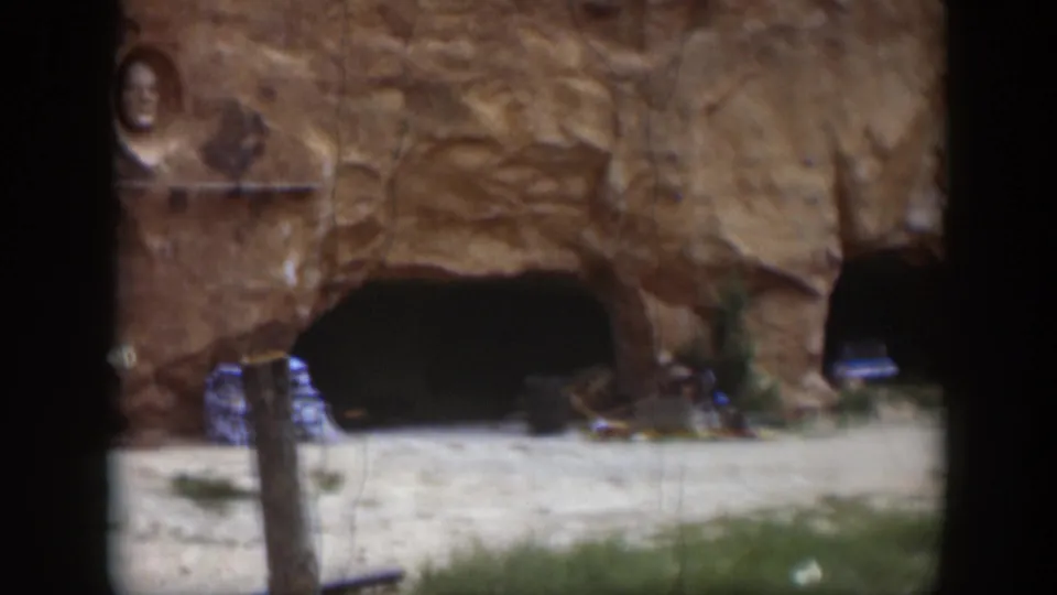 1951 Utah frame showing a large cave-like opening, a parked car partly visible at the right edge, and a foreground post.