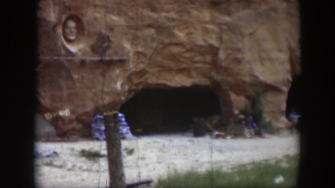 Sandstone wall with carved face above a dark cave opening and pale ground.