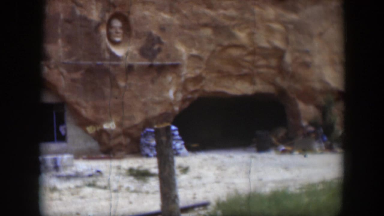 1951 Utah home-movie frame of sandstone with a carved face above a cave-like recess and rough stonework nearby.